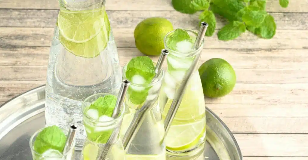 A pitcher and glasses filled with water, lime slices, and mint leaves on a silver tray.