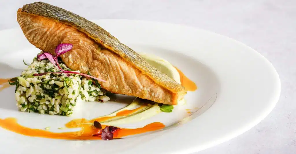 A cooked salmon fillet served with a side of green rice and garnished on a white plate.