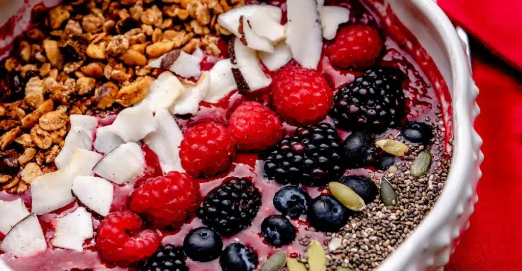 A bowl filled with various berries, granola, coconut flakes, and seeds.