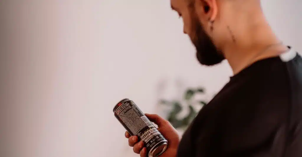 A man with a beard looking at the label of a black can.