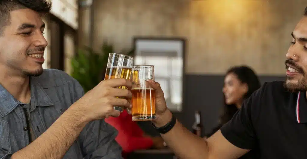 Two men toasting with glasses of beer at a table in what appears to be a bar or restaurant.