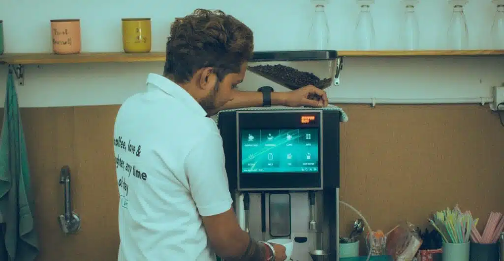 A coffee shop worker wearing a white polo shirt operating a smart coffee maker.