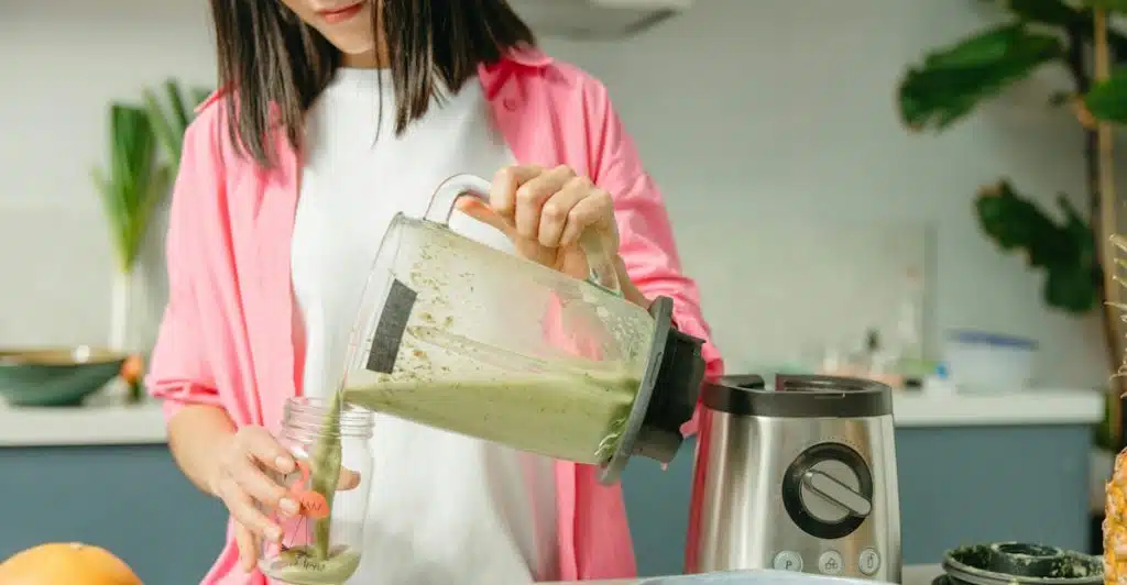 A person pouring a green liquid from a blender into a glass jar.