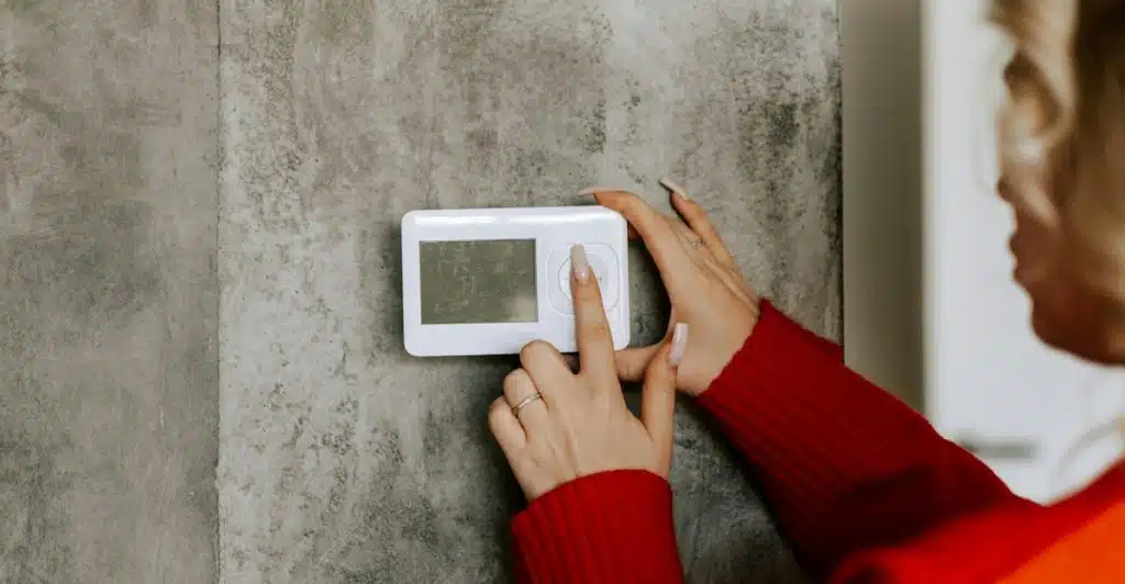 A person's hands adjusting a white smart lighting thermostat on a wall.