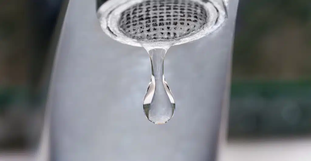 Close-up of a dripping faucet with a large drop of water about to fall.