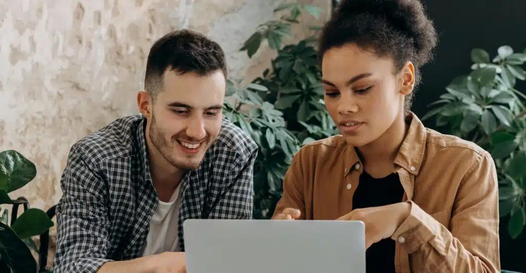 A man and a woman sitting together, looking at a laptop screen and smiling.
