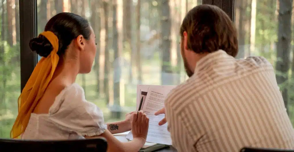 A man and a woman sitting at a desk, looking at documents together.