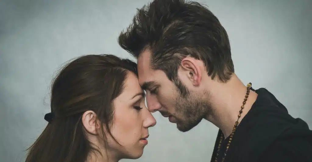 A man and a woman with their foreheads touching and eyes closed, facing each other.