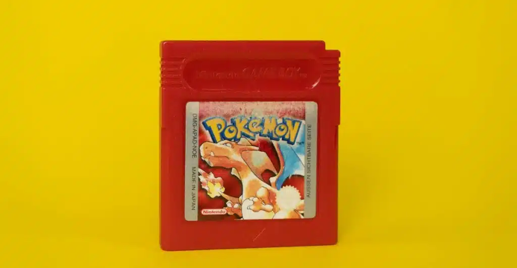 A red Nintendo Game Boy cartridge for the game Pokémon Red, featuring Charizard on the label, against a yellow background.