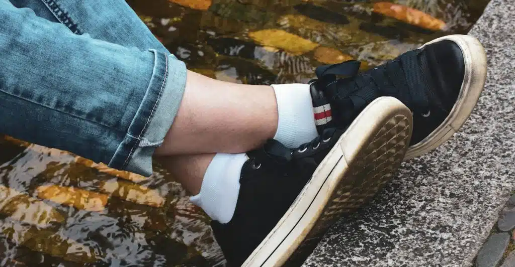 A person sitting with cuffed jeans and black sneakers with white socks.