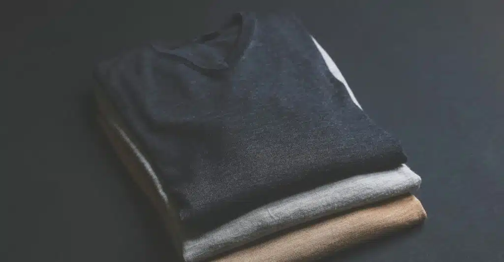 A stack of three folded textured sweaters in dark gray, light gray, and brown.