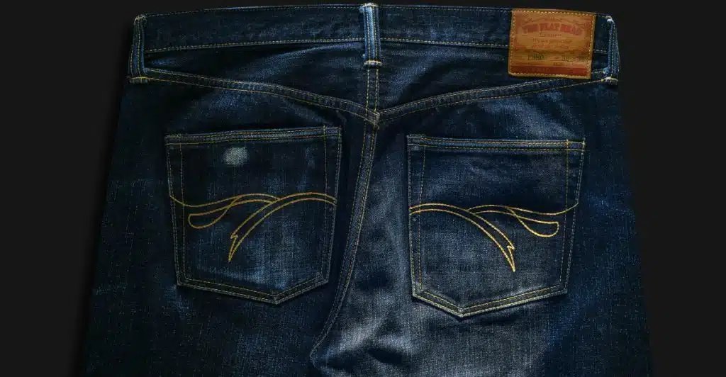 A close-up of the back pockets and waist of a pair of dark wash jeans