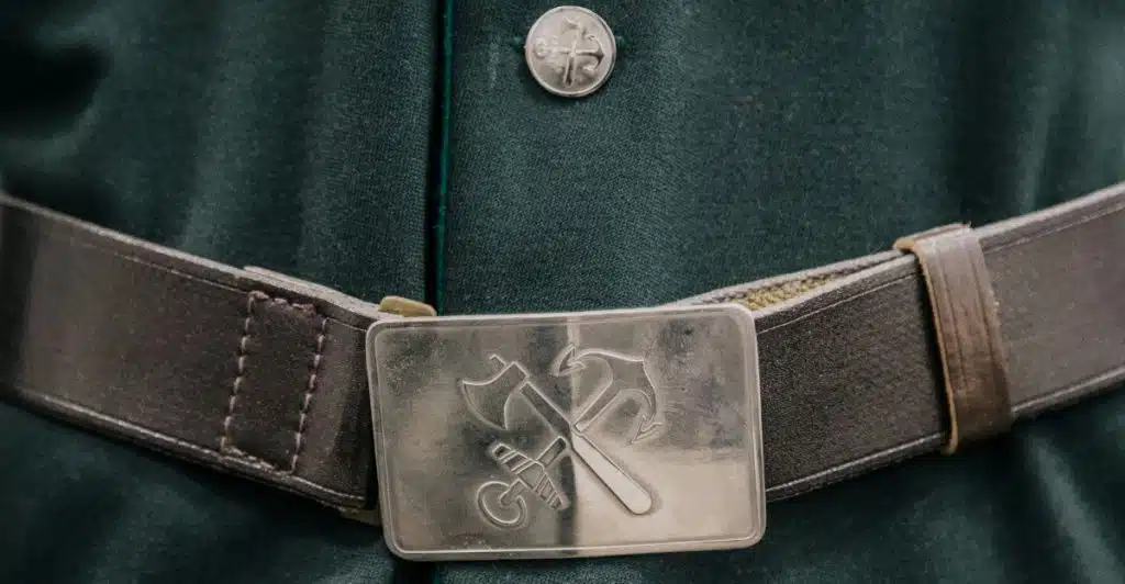 A close-up of a silver belt buckle with an axe design on a dark belt.
