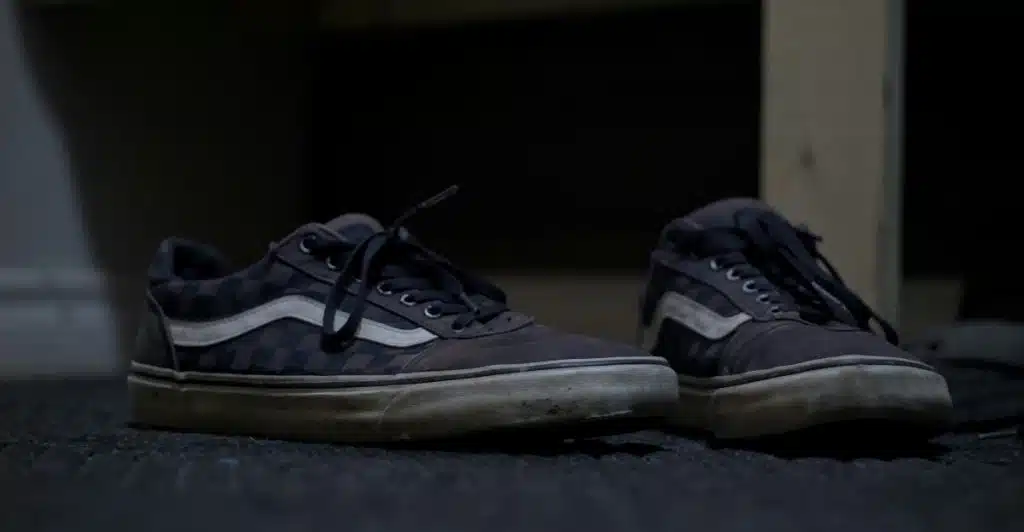 A pair of faded and worn dark checkered sneakers with white soles.