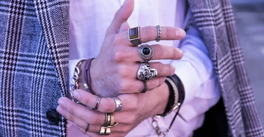 A hand adorned with multiple rings and bracelets, wearing a plaid blazer and white shirt.