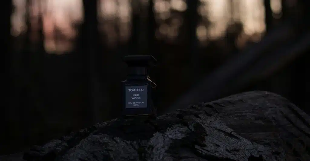 A Tom Ford Oud Wood fragrance bottle on a tree trunk in a forest setting.