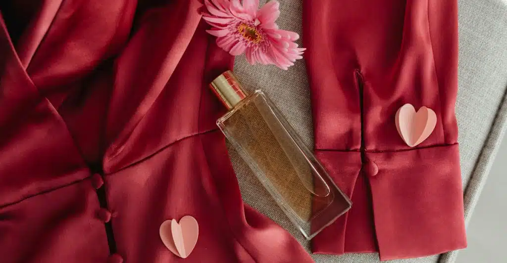 A Maison Francis Kurkdjian Baccarat Rouge 540 fragrance bottle on a red silk robe with pink paper hearts and a pink flower.