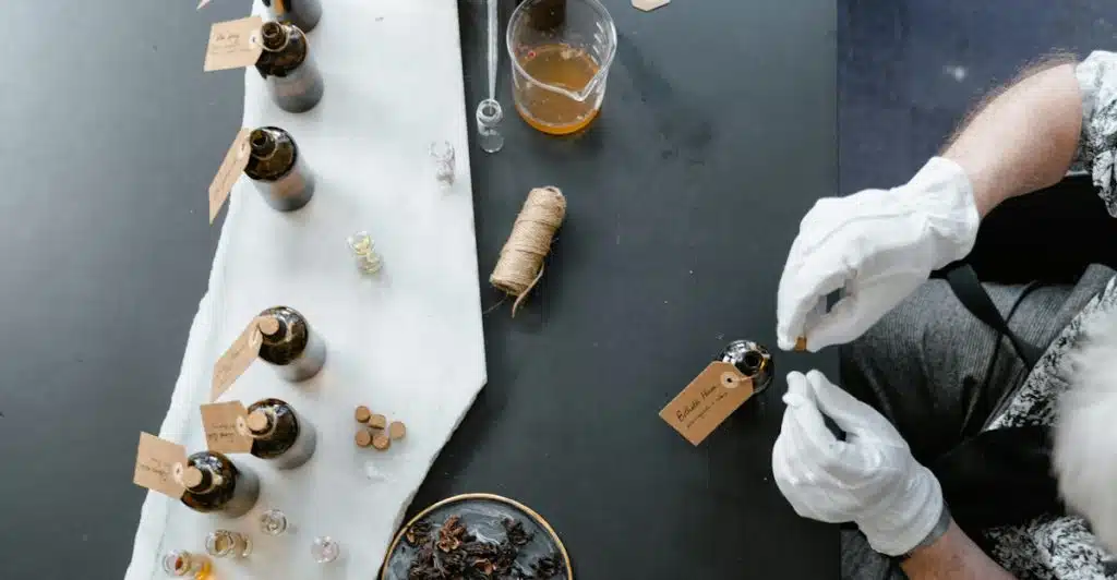 A person in white gloves working with various fragrance bottles and ingredients on a table.