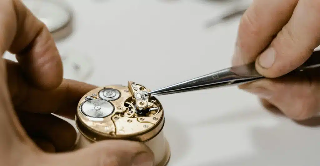 A person's hands meticulously working on the intricate internal components of a mechanical watch using tweezers.