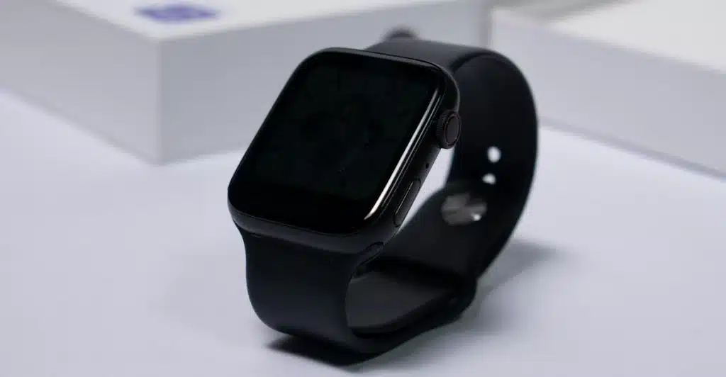 A black smartwatch with a dark screen and a black band resting on a white surface.