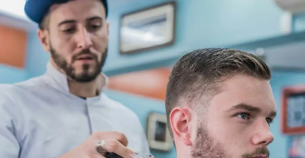 A barber dusting off a man's neck with a brush after a haircut.