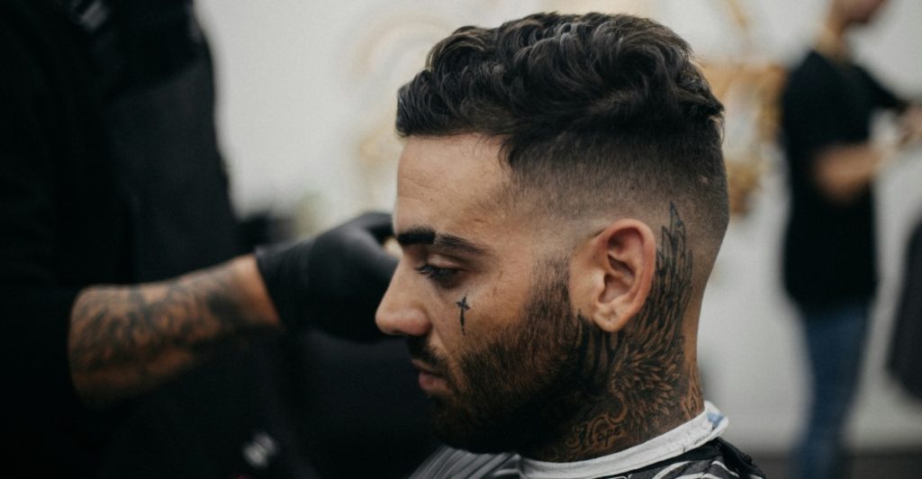 A man with a textured crop haircut with tattoos on his neck and face.