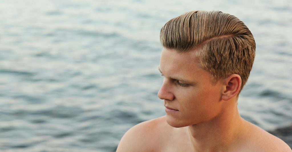 A man with a low fade with pompadour haircut looking at the ocean.