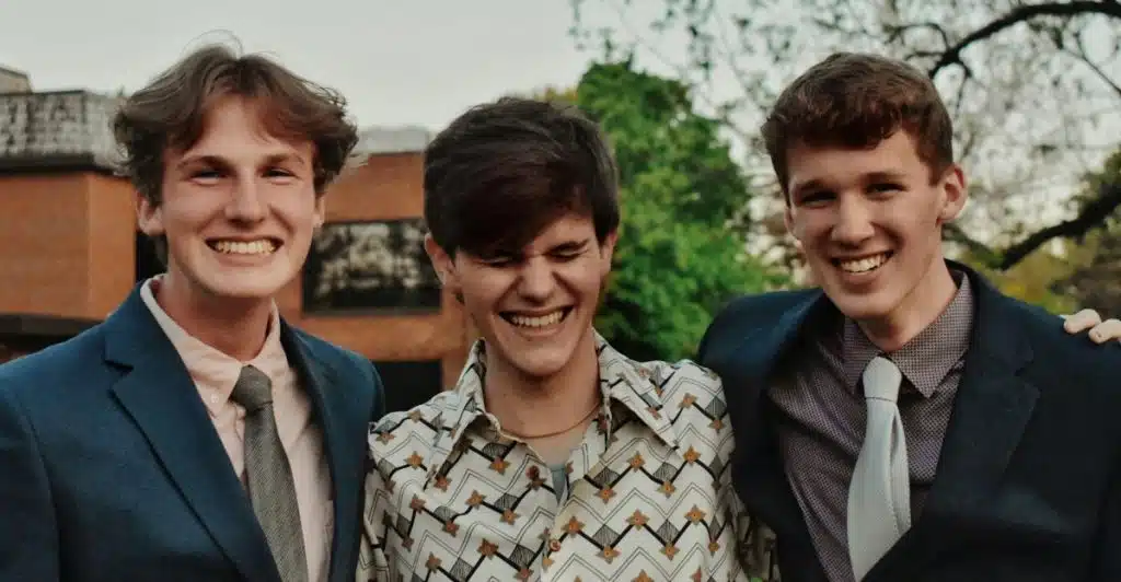 Three men with natural waves hairstyles, two in suits and one in a patterned shirt, smiling outdoors.