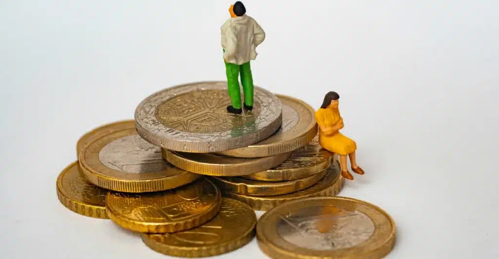 Two small figurines, one appearing to be a man standing and the other a woman sitting, placed on separate stacks of euro coins.