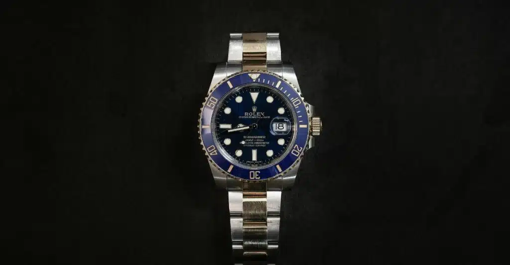 A close-up shot of a two-tone Rolex Oyster Perpetual watch with a blue dial and bezel, resting on a dark, plain background.