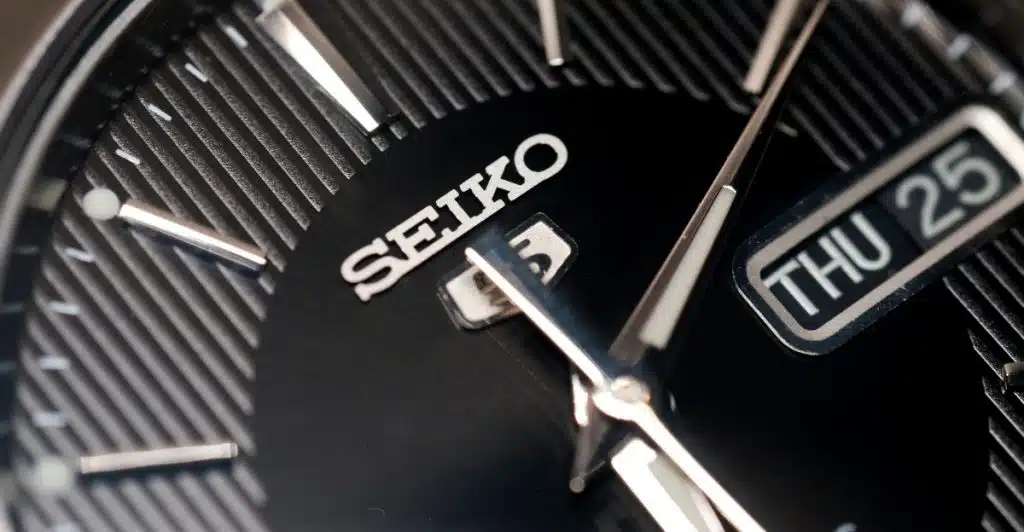 A close-up of a Seiko Presage Cocktail Time watch face, showcasing a black dial with a sunburst pattern, silver hands, and a date window.