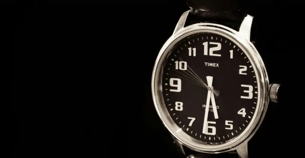 A close-up of a Timex Marlin Hand-Wound watch with a black dial, large white Arabic numerals, and a black leather strap, on a dark background.