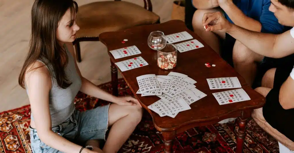 Three people gathered around a wooden table, playing a game with cards and small tokens.