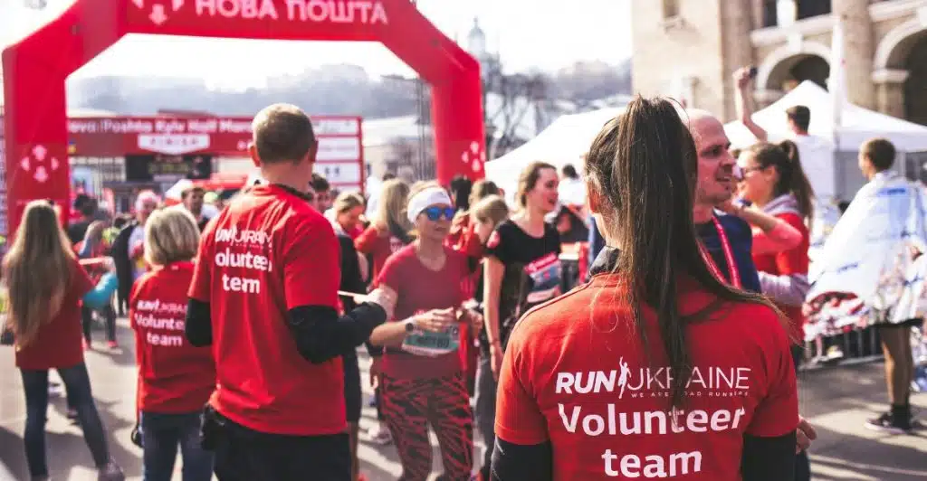 A group of people wearing red "Volunteer team" shirts gathered outdoors at what appears to be a race event.