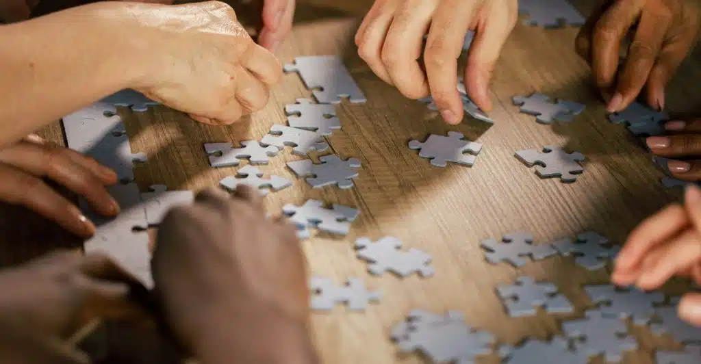 Several hands collaborating to assemble a jigsaw puzzle on a wooden table.