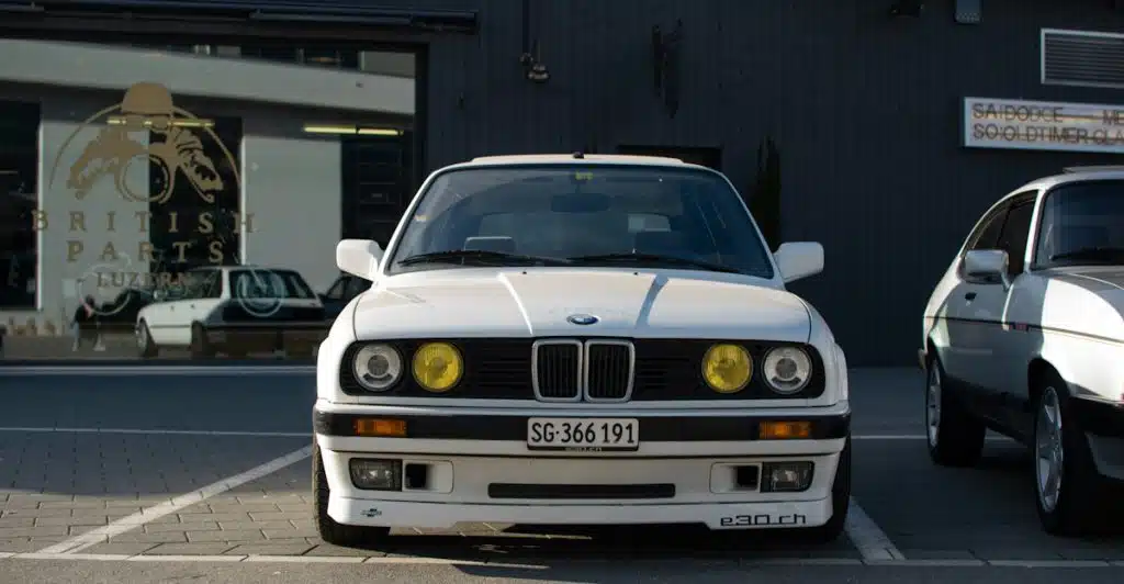 A white 1990 BMW E30 M3 parked facing forward, with a building in the background.