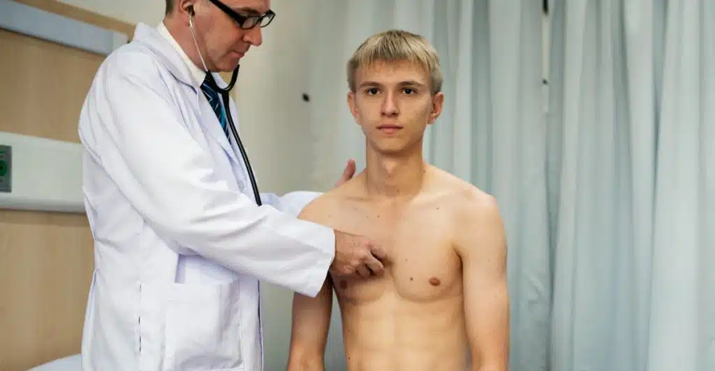 A doctor using a stethoscope to examine a young man's chest during a checkup.