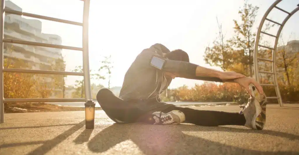 A man stretches post-workout in the park with the sun on his back.