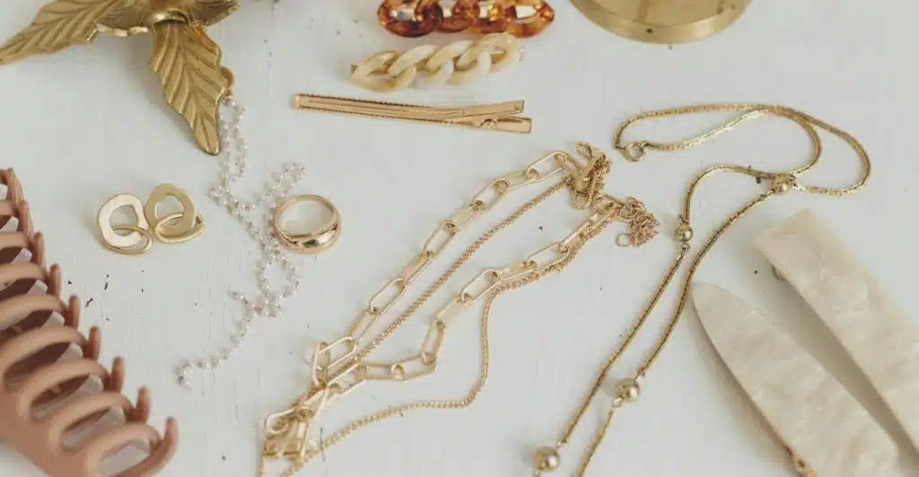 A collection of gold necklaces, pearl earrings, rings, and various hair clips are displayed on a white surface.