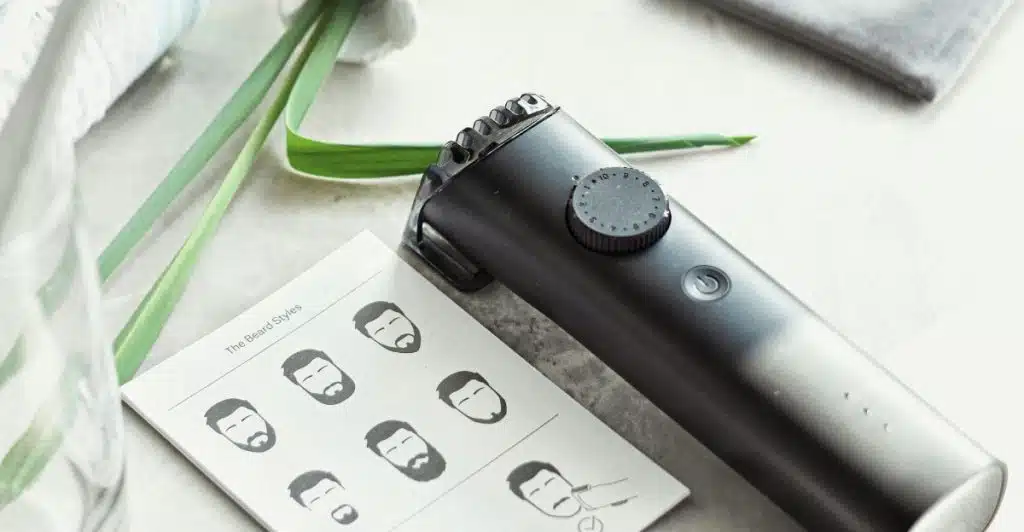 An electric beard trimmer is placed next to a small booklet showing different beard styles, with green plants in the background.