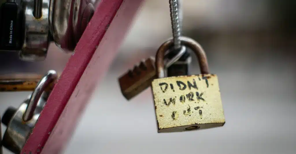 A padlock with "Didn't work out" written on it, hanging from a metal structure.