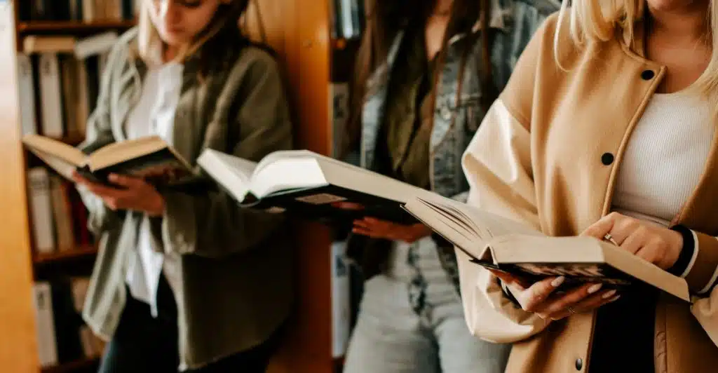 Three people standing in a library, each holding an open book and reading