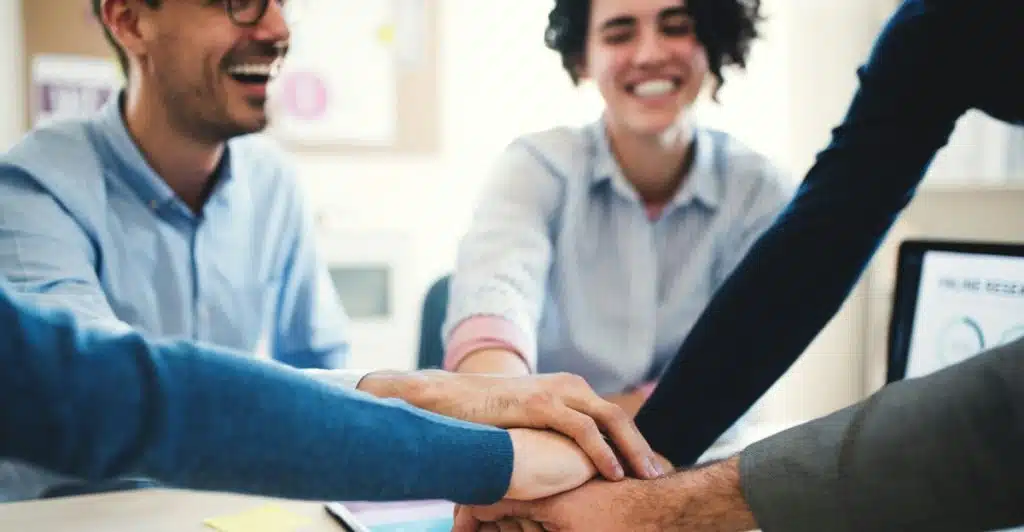 Four coworkers putting their hands together in a gesture of teamwork over a table with documents