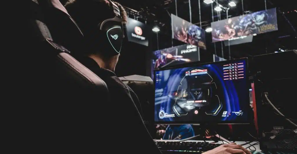 A man wearing headphones is sitting in a gaming chair and playing a video game on a monitor.