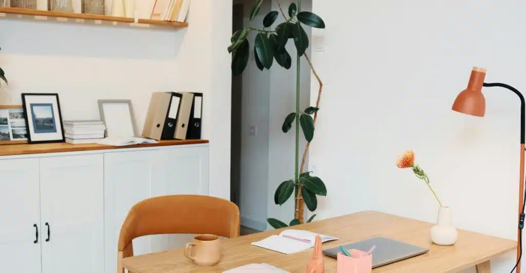 A stylish home office setup with a wooden desk, a plant, and an orange lamp, next to a white cabinet