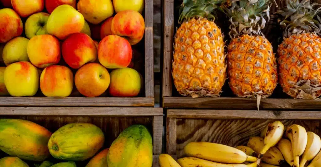 Four wooden crates are filled with various fresh fruits, showcasing piles of red and yellow apples, ripe pineapples, green papayas, and bunches of yellow bananas.