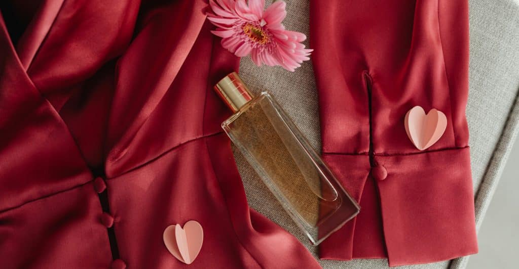 A Maison Francis Kurkdjian Baccarat Rouge 540 fragrance bottle on a red silk robe with pink paper hearts and a pink flower.