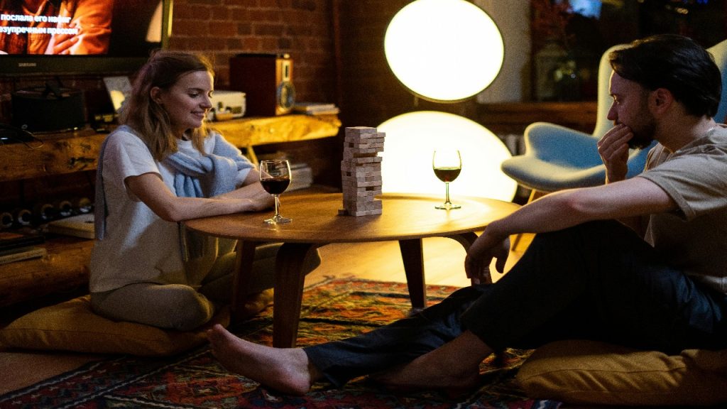 A couple playing a game of Jenga at a round wooden table.