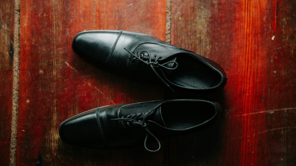 A pair of black dress shoes on a wooden floor.