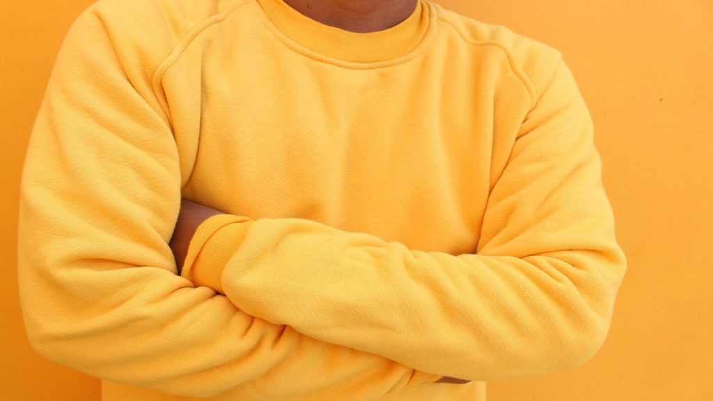A man wearing a yellow sweatshirt with his arms crossed.